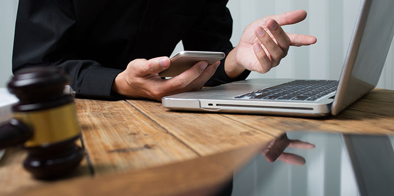 Man Looking at Phone and Laptop with a Gavel on the Table